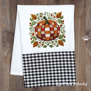 May include: White kitchen towel with a black and white checkered border. The towel features an embroidered design of a pumpkin with orange and red stripes surrounded by green leaves and vines.