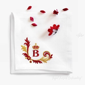 May include: White linen napkin with a red and gold embroidered monogram featuring the letter "B" with a crown above it. The monogram is surrounded by a decorative floral design.
