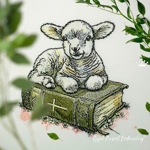 Può includere: Ricamo di un agnello bianco seduto su un libro verde con una croce sulla copertina. Il libro è circondato da piccoli fiori rosa.