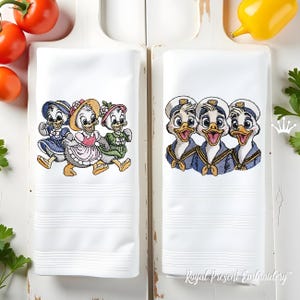 Könnte beinhalten: Zwei weiße, bestickte Küchentücher. Eines zeigt drei Entenküken in Kleidern und Mützen, das andere drei Entenküken in Matrosenmützen und -uniformen. Die Handtücher haben horizontale, genähte Linien.