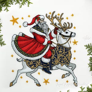 Può includere: Disegno ricamato di Babbo Natale che cavalca una renna bianca con accenti dorati e blu. Il disegno è circondato da stelle dorate.