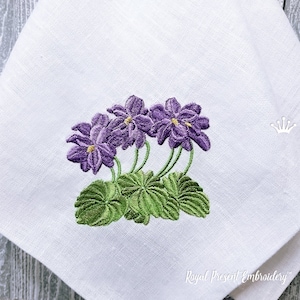 May include: Embroidered design of three purple violets with green leaves on a white fabric background.