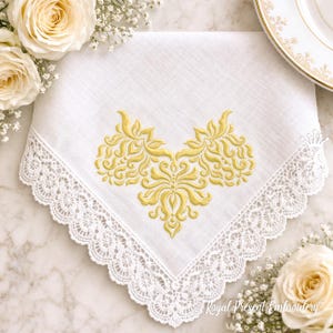 Pode incluir: Lenço branco com uma delicada borda de renda e um design de bordado floral dourado. O lenço é cercado por rosas brancas e pequenas flores brancas, criando uma estética elegante e clássica.