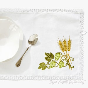 以下が含まれることがあります： 緑のつる植物と黄色の小麦の刺繍が施された白いテーブルランナー。デザインはランナーの右下隅にあります。