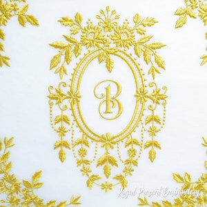 May include: Gold embroidered monogram featuring the letter B within a decorative oval frame, surrounded by floral and leaf designs. The design is on a white background.