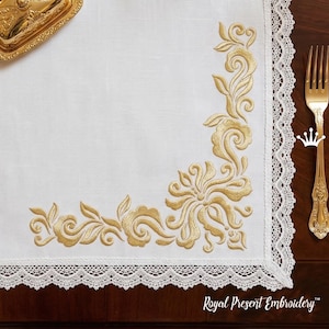 May include: White linen table runner with gold floral embroidery in the corner. The embroidery features a detailed design of flowers and leaves. The edge of the runner is trimmed with white lace. A gold fork is on the right side.