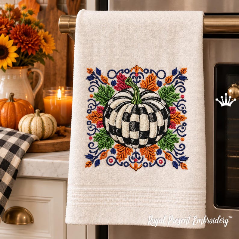 Puede incluir: Un pa&ntilde;o de cocina blanco con un dise&ntilde;o bordado de una calabaza a cuadros blancos y negros rodeada de coloridas hojas de oto&ntilde;o en tonos naranja, verde y azul, con el texto Royal Present Embroidery en la esquina inferior.