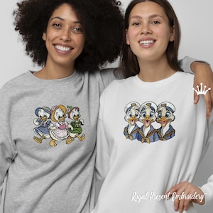 Könnte beinhalten: Zwei Sweatshirts, eines grau und eines weiß, jeweils mit gestickten Cartoon-Entenfiguren. Das graue Sweatshirt hat drei Enten in Kleidern, während das weiße drei Enten in Matrosenoutfits zeigt. Der Text "Royal Present Embroidery" befindet sich unten.