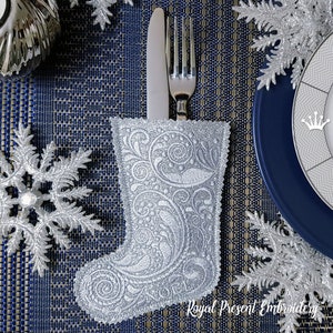 May include: Silver Christmas stocking with a white floral design, used as a cutlery holder for a fork and knife on a blue and gold placemat. The text "Royal Present Embroidery" is visible at the bottom of the image.