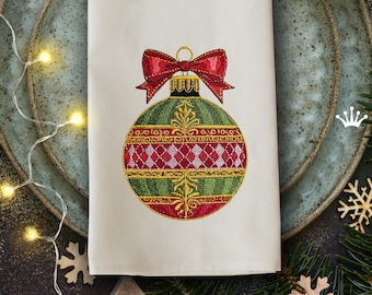 Peut inclure: Motif de décoration de Noël brodé représentant une boule verte et rouge avec des accents dorés et un nœud rouge. Le motif est sur un fond de tissu blanc.