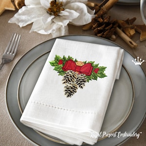 May include: A white linen napkin with an embroidered design of pine cones, holly leaves, and a red bow. The design is centered on the napkin and is surrounded by a dotted border.