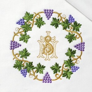 Pode incluir: Um monograma bordado a ouro das letras "IHS" rodeado por uma coroa de folhas verdes e uvas roxas.