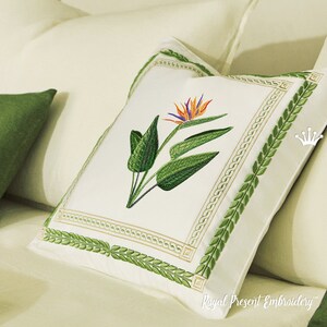 May include: A white pillow with a green embroidered border featuring a leafy design. The center of the pillow features an embroidered bird of paradise flower with orange, yellow, and blue accents.