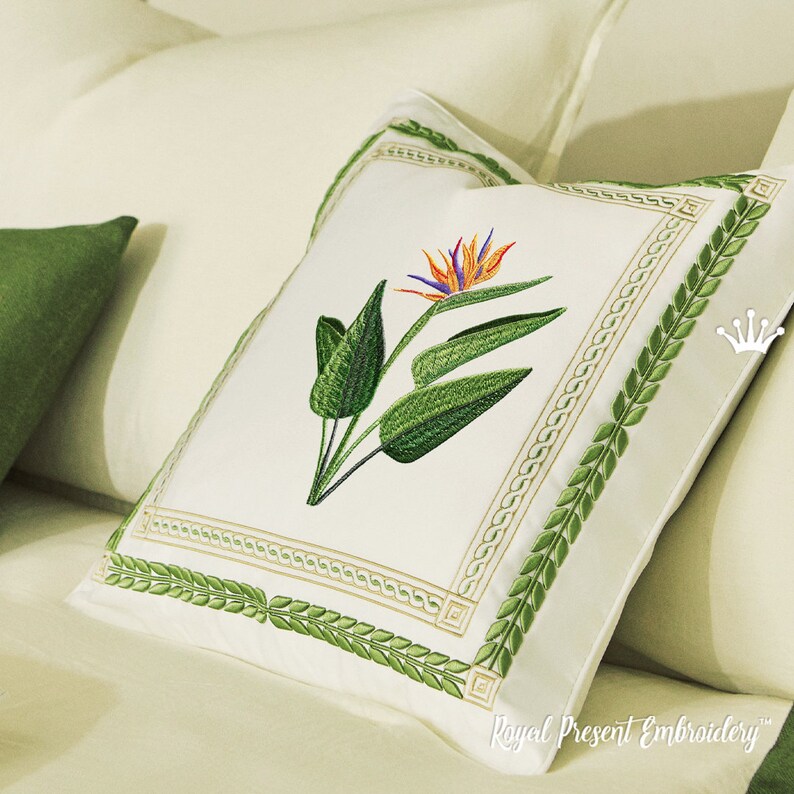 May include: A white pillow with a green embroidered border featuring a leafy design. The center of the pillow features an embroidered bird of paradise flower with orange, yellow, and blue accents.