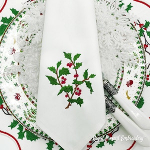 May include: A white linen napkin with a green holly sprig and red berries embroidered on it. The napkin is folded and placed on a white plate with a green and red holiday design.