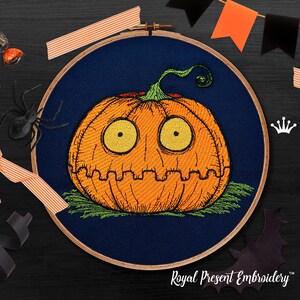 May include: Embroidered pumpkin with a surprised expression, stitched in orange, yellow, and green thread on a dark blue fabric background. The embroidery is framed in a wooden hoop.