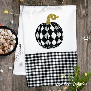 May include: A white kitchen towel with a black and white checkered border. The towel features an embroidered black and white pumpkin with a gold stem.
