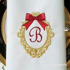 Può includere: Tovagliolo di stoffa bianco con cornice dorata ricamata, fiocco rosso e lettera "B". La cornice ha un design ornato. Il testo "Royal Present Embroidery" è in basso a destra.