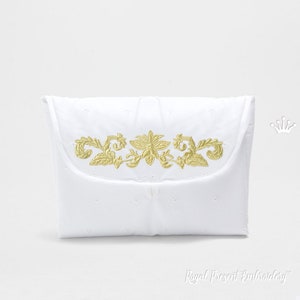 May include: White cloth nappy bag with a gold embroidered floral design. The bag has a flap closure and is made of a soft, quilted fabric.