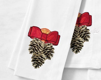 Könnte beinhalten: Zwei weiße bestickte Küchentücher mit einem Design aus Tannenzapfen und roter Schleife. Der Tannenzapfen ist mit einem kleinen orangenen Kreis verziert. Die Handtücher sind gefaltet und übereinander gestapelt. Der Text "Royal Present Embroidery" ist am unteren Rand des Bildes sichtbar.
