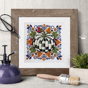 Puede incluir: Un dise&ntilde;o de bordado cuadrado que presenta una calabaza central con un patr&oacute;n de cuadros blanco y negro, rodeada de coloridas hojas de oto&ntilde;o en tonos naranja, amarillo y verde, enmarcada por intrincados adornos azules y detalles rojos.