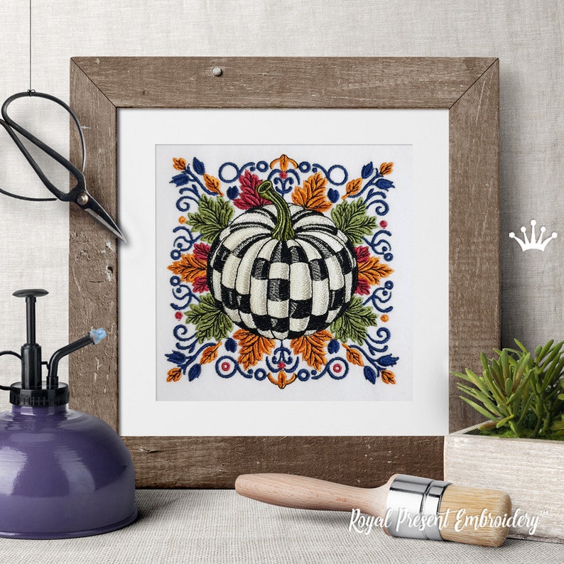 Puede incluir: Un dise&ntilde;o de bordado cuadrado que presenta una calabaza central con un patr&oacute;n de cuadros blanco y negro, rodeada de coloridas hojas de oto&ntilde;o en tonos naranja, amarillo y verde, enmarcada por intrincados adornos azules y detalles rojos.