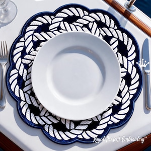 May include: A round navy blue placemat with a scalloped edge and a white embroidered rope pattern. A plain white dinner plate is centred on the placemat, flanked by a silver fork on the left and a silver knife on the right side.