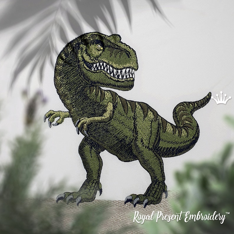 May include: Green embroidered dinosaur with a crown above its tail. The dinosaur is standing on a beige surface.