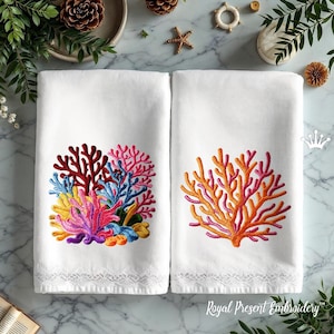 May include: Two white hand towels with embroidered coral reef designs. One towel features a colorful coral reef in shades of red, pink, blue, yellow, and purple. The other towel has an orange and pink coral reef design. Both towels have a lace trim.