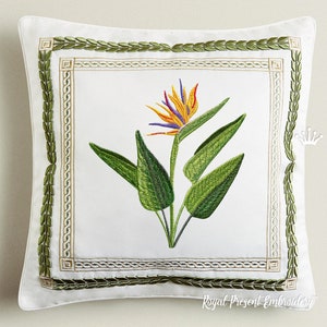 Puede incluir: Almohada blanca con un borde de laurel verde y una flor de ave del paraíso bordada en el centro. La flor es naranja, amarilla, morada y azul.