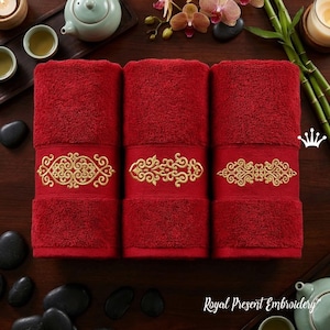 May include: Three red bath towels with gold embroidered decorative bands. The towels are arranged on a dark wooden surface, with tea cups, a teapot, and spa elements in the background. The text "Royal Present Embroidery" is visible.