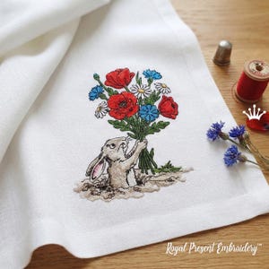 May include: Embroidered white linen napkin featuring a rabbit holding a bouquet of red poppies, blue cornflowers, and white daisies. The design includes the text "Royal Present Embroidery". A thimble and spool of red thread are in the background.