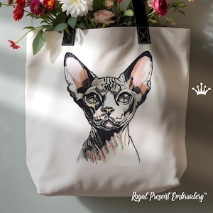 Puede incluir: Una bolsa de tela blanca con asa negra y una imagen bordada de un gato Sphynx. El gato mira directamente al espectador con una expresión seria. La bolsa tiene el texto "Royal Present Embroidery" en la parte inferior.