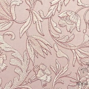 May include: A pink fabric with a delicate floral embroidery pattern. The design features intricate leaves and flowers in a light pink color.