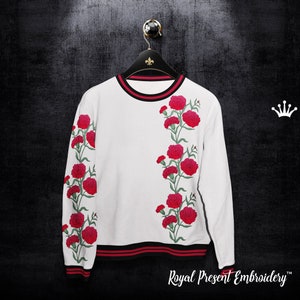 May include: White long-sleeve sweatshirt with red carnation embroidery on the sleeves and right side of the chest. The sweatshirt has black and red stripes around the bottom hem.