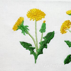 Pode incluir: Desenho bordado de tr&ecirc;s dentes-de-le&atilde;o amarelos com folhas e caules verdes. O desenho est&aacute; sobre um fundo de tecido branco. O texto "Royal Present Embroidery" &eacute; vis&iacute;vel no canto inferior direito.
