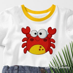 May include: A white t-shirt with a yellow trim around the neck. The t-shirt has an embroidered red crab with yellow accents and large white eyes.