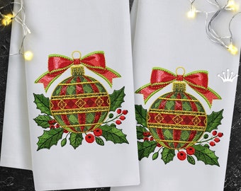 Peut inclure: Deux serviettes à main blanches sur le thème de Noël. Chaque serviette présente un motif de décoration brodée avec des rayures rouges et vertes, un nœud rouge et des feuilles de houx avec des baies rouges. Les serviettes sont décorées d'accents dorés.