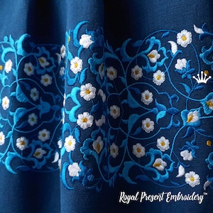 Op de afbeelding: Close-up van een blauwe stof met witte en blauwe geborduurde bloemenmotieven. De borduursels tonen ingewikkelde patronen van bladeren en bloemen.