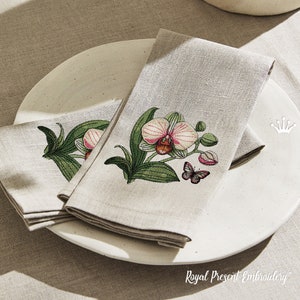 May include: Two linen napkins with embroidered orchid flowers and a butterfly. The napkins are folded and placed on a white plate. The text "Royal Present Embroidery" is visible at the bottom of the image.