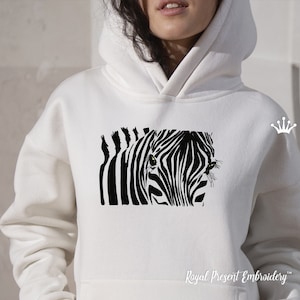 以下が含まれることがあります： 白地に黒と白のシマウマ柄がプリントされた白いフード付きスウェットシャツ。シマウマの目がプリントに映っています。