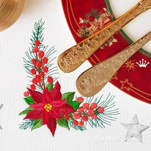 May include: Embroidered Christmas corner design featuring a poinsettia flower, pine branches, and red berries. The design is stitched on a white fabric background.