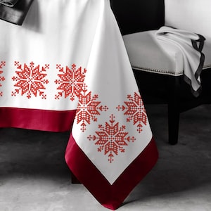 May include: White tablecloth with a red border and red embroidered snowflake designs.