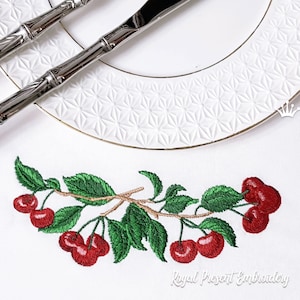 Pode incluir: Desenho bordado de um ramo de cerejeira com cerejas vermelhas e folhas verdes. O desenho está sobre um fundo de tecido branco.