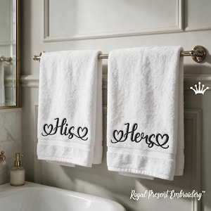 Puede incluir: Dos toallas de baño de algodón blanco colgadas en un toallero metálico. Cada toalla presenta texto bordado en negro con detalles de corazones decorativos. La toalla izquierda muestra la palabra His y la derecha la palabra Hers en cursiva.