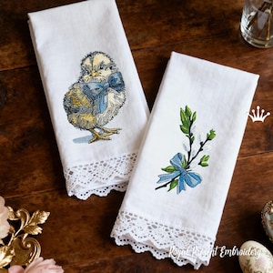May include: Two white linen towels with embroidered designs. One features a detailed chick with a blue bow, the other a branch with green leaves, white buds, and a blue bow. Both have a white lace trim.