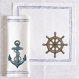 Puede incluir: Un juego de dos servilletas de lino blanco con bordes bordados azules. Una servilleta presenta un ancla azul con una cuerda, y la otra presenta un timón de barco dorado con un centro azul.