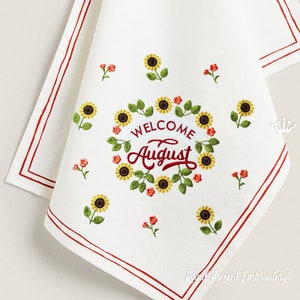 Könnte beinhalten: Weißes Küchentuch mit rotem besticktem Rand und einem Kranz aus Sonnenblumen mit dem Text "Willkommen August" in Rot.