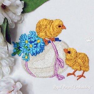 May include: Embroidered design of two yellow chicks with a white egg decorated with blue flowers and a pink ribbon. The design is on a white fabric background.