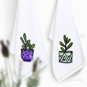 Puede incluir: Dos toallas de cocina bordadas con un diseño de planta verde en una maceta. Una toalla presenta una maceta morada con lunares blancos y la otra una maceta verde con un patrón geométrico.